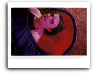 an instant picture of m in a blue and red sleeping bag with a papier-machéd newspaper mask over her face