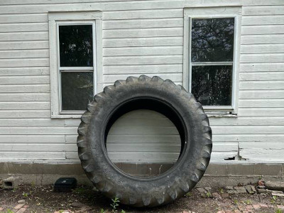 big tire propped up against a white house between two windows