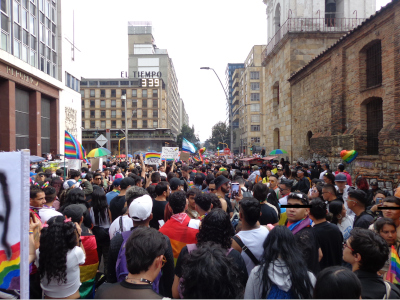 a big crowd of people and rainbows marching in bogotá with the el tiempo building in the background